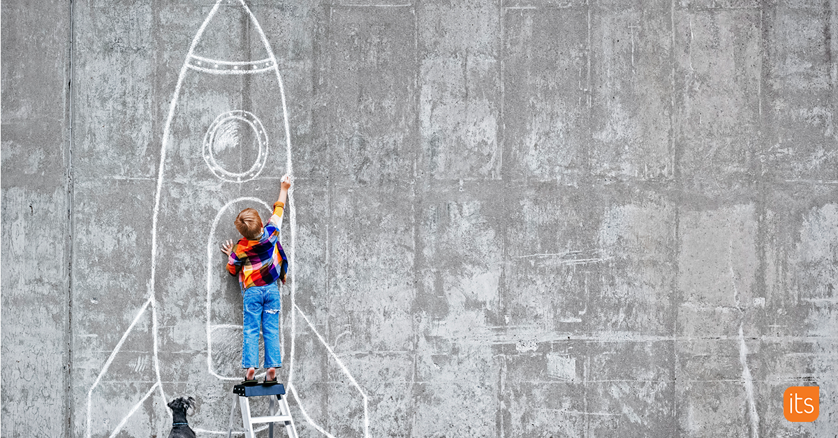 Foto van een Leerling die voor een betonnen muur staat met een krijtstift in de hand en een raket tekent.